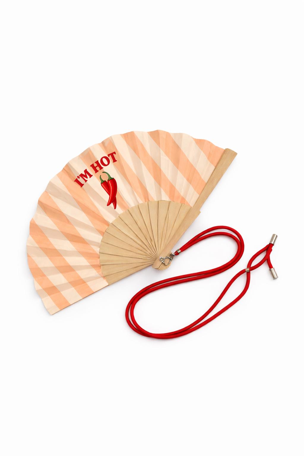 Éventail pliable en bois et textile rayé, décoré du message « I’M HOT » et d’un motif piment. Il est équipé d’un lien ajustable pour le porter autour du cou ou au poignet, parfait pour les fortes chaleurs.
