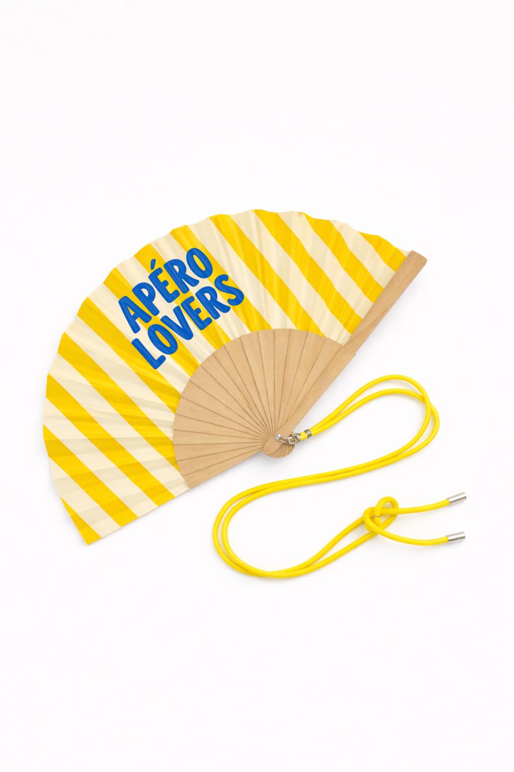 Éventail APÉRO LOVERS déplié avec son lien ajustable jaune.
Sa structure en bois naturel et son motif rayé en font un accessoire léger, pratique et résistant.
Parfait pour se rafraîchir lors des apéros, festivals ou vacances au soleil.