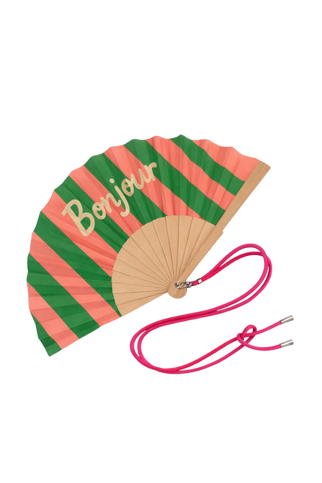 L’éventail Bonjour déployé dévoile ses rayures vertes et corail ainsi que son message chaleureux.
Sa structure en bois naturel et son lien ajustable en font un accessoire à la fois pratique et stylé pour l’été.