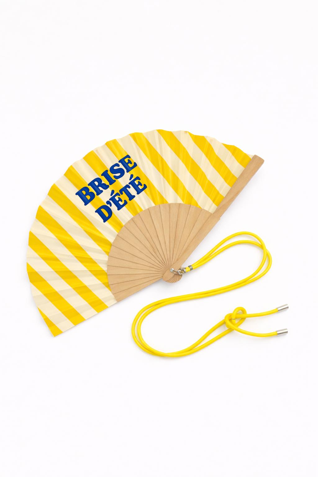 Éventail Brise d’été présenté avec sa boîte cadeau rayée jaune et écru, assortie au design de l’éventail, idéal pour offrir.
