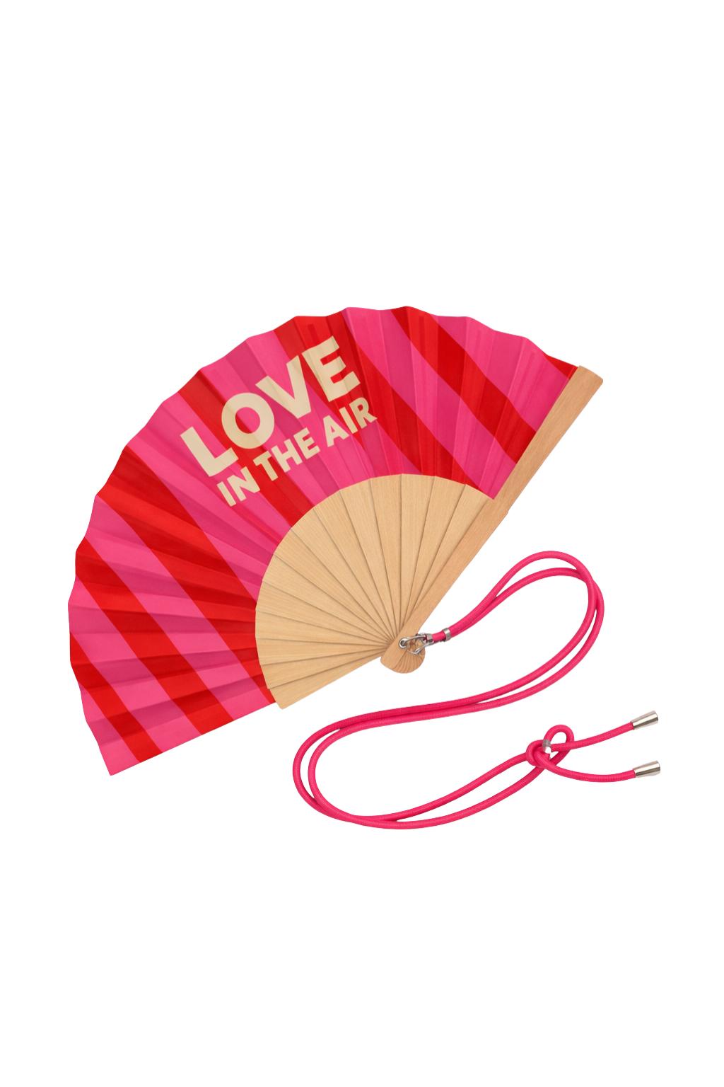 L’éventail LOVE IN THE AIR déployé, avec son lien ajustable.
Motif rayé rose et rouge, message assumé et structure en bois naturel : l’accessoire indispensable pour rester cool avec style.
